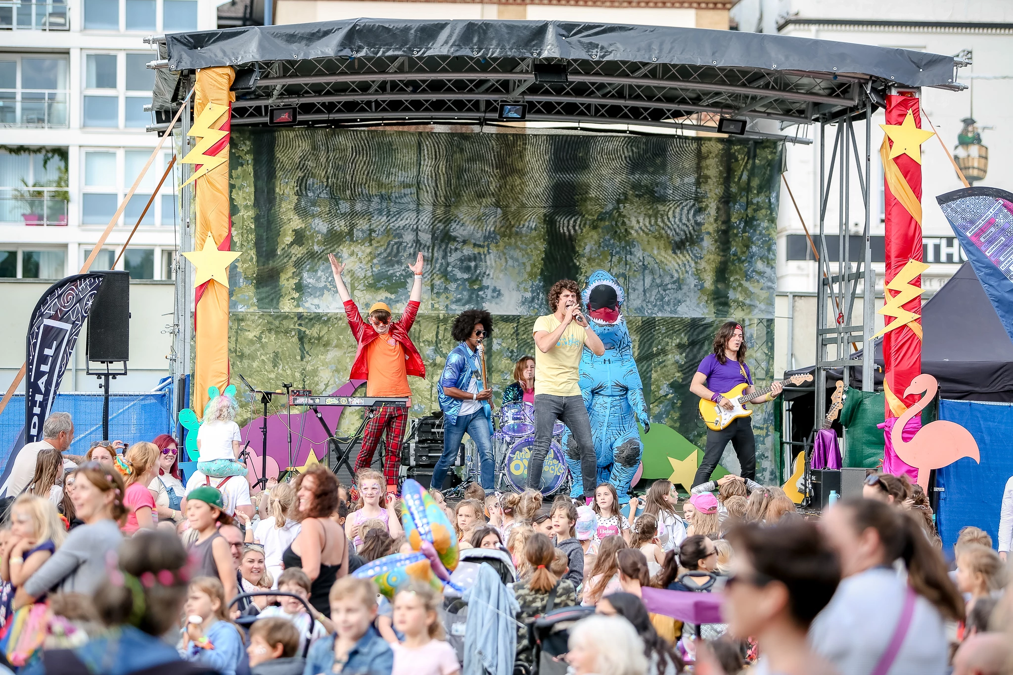 Image of band with one member dressed as a dinosaur playing to a crowd of children at Victorious Festival